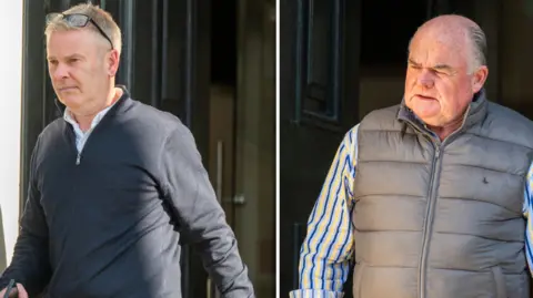 Martin McKeown Two men. The one on the left is wearing a white shirt under a dark zip-up top and light blue trousers. He is wearing a watch on his left wrist and carrying a mobile phone in his right hand. The man on the right is wearing a blue and yellow striped shirt with the sleeves rolled up under a zip-up grey sleeveless top. He has a silver bracelet on his right wrist