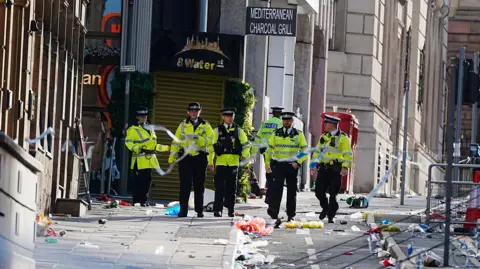PA Media Water Street covered in debris as six police officers can be seen close to the police cordon after the incident on 26 May