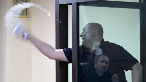 Reuters A man behind a glass window is pictured throwing water out of a glass