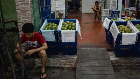 Getty Images Two men at a fruit stall sitting on the ground, using their phones