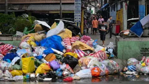 Getty Images A pile of multi-coloured rubbish on a street. There are people walking behind it.