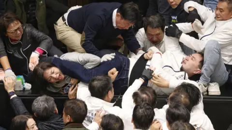 Getty Images Legislators from various political parties wearing dark or light coloured jackets brawl in the Taiwan legislature, with several people trying to pull apart other people in the middle physically fighting with each other