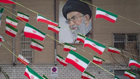 NurPhoto via Getty Images A mural of Iran's Supreme Leader Ayatollah Ali Khamenei is seen on the side of a  building in Azadi avenue with reams of Iranian national flags hanging in the foreground, in Tehran on 11 February 2022.