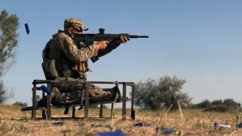 Lee Durant/BBC A Ukrainian soldier fires a shotgun in a field during training