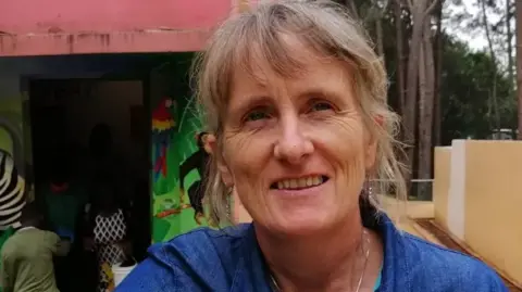 Universtity of Limerick Gena Heraty pictured outside an orphanage in Haiti. She is wearing a blue shirt and has light blonde and silver hair, which is mostly pinned back.