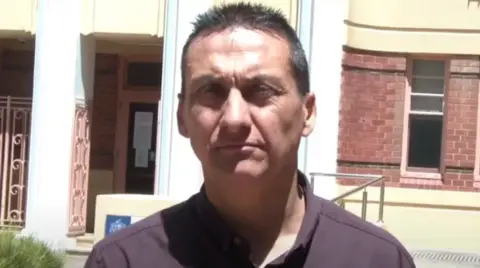 Supplied Dezi Freeman is looking straight down the barrel of the camera. He is wearing a maroon shirt and has short grey hair. He is squinting because of the sun, and an official building is behind him - likely a court house.