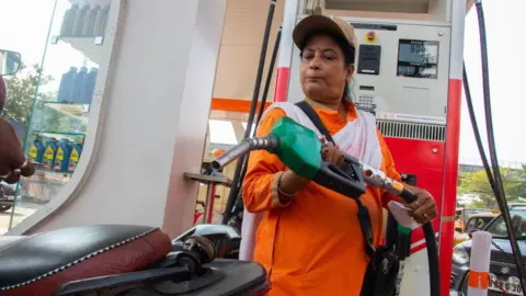 Getty Images A petrol pump worker, in a saffron dress, putting fuel in a bike. The pumping machine can be seen in the background.

