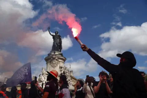 Reuters A man holds a flare aloft against the backdrop of a statue, a blue sky and crowd