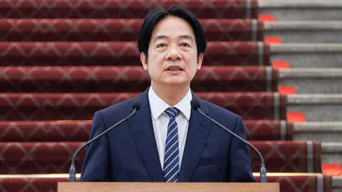 Getty Images Taiwan's President Lai Ching-te stands in front of a microphone dressed in a dark blue suit and striped tie