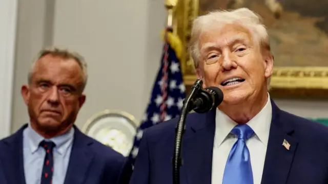 Donald Trump (r) wearing a blue suit and blue tie stands next to and slightly in front of Robert F Kennedy Jr who is wearing a blue suit, blue shirt and patterned tie