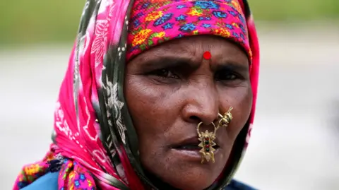 Reuters Kali Devi, 38, a migrant worker from Nepal, waits next to a helipad, hoping for news of her missing children and relatives from Dharali after it was struck by landslides, in Bhatwadi village in the northern state of Uttarakhand, India, August 7, 2025.