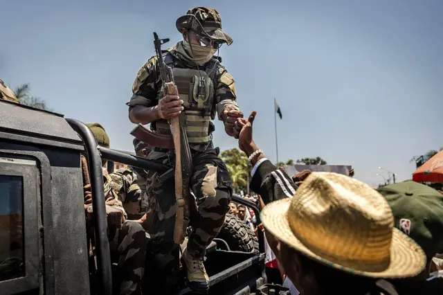 A member of a Malagasy Army unit riding on a patrol vehicle exchanges a fist bump with a civilian as residents gather for a civil society rally outside City Hall in Antananarivo, on October 13, 2025