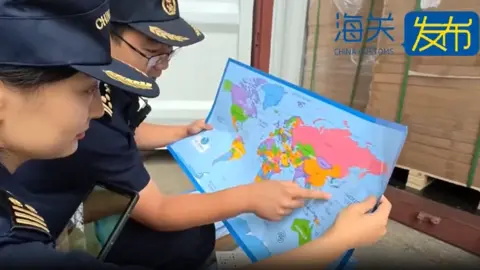 China Customs Two customs officers wearing dark blue uniform squatting on the ground and looking at a map. One of them is pointing at an area near China on the map