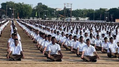 BBC Hundreds of RSS volunteers sit in straight lines wearing a white shirt and khaki trousers