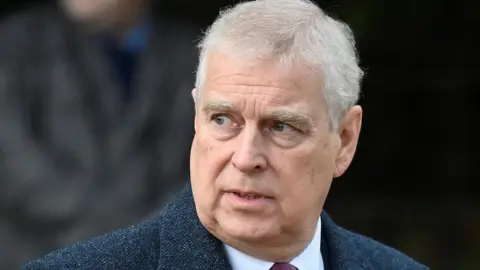 Reuters Prince Andrew has short grey hair and is gazing to one side. He is wearing a dark blue jacket, a white shirt and a red tie.