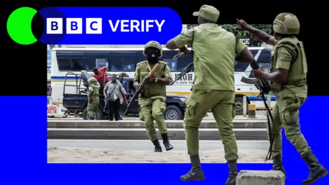 Getty Images Armed Tanzanian police stand in the streets as demonstrations continue around them. 