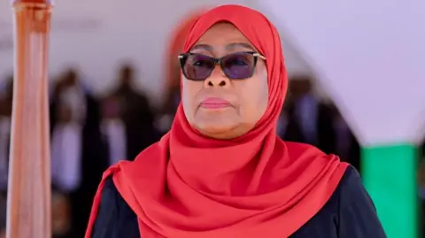 Reuters A close-up of Samia Suluhu Hassan wearing dark glasses and a red headscarf.