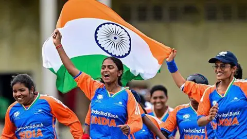 AFP via Getty Images A group of visually challenged women cricketers who are part of the India team, celebrate a victory in the inaugural Blind Women’s T20 Cricket World Cup - wearing their blue and saffron jerseys and waving the Indian flag. 