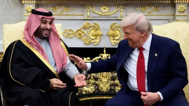 Trump and Bin Salman face one another in the Oval Office laughing.Trump extends his hand towards the crown prince