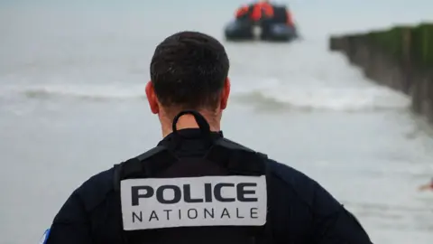 Getty Images A French policeman looks at a migrant wading to the shore after attempting to cross the English Channel to reach Great Britain on a smuggler's inflatable dinghy at Sangatte beach near Calais, northern France, on January 15, 2025