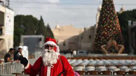 EPA A man dressed as Santa Claus stands in Manger Square ahead of the lighting of the Christmas tree in the West Bank city of Bethlehem