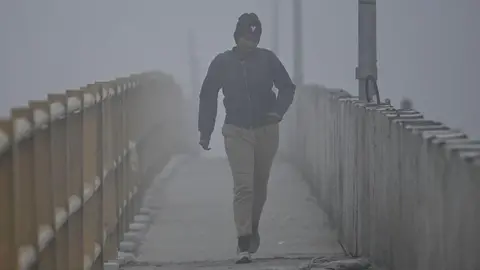 AFP via Getty Images A woman - wearing jacket, joggers and a headgear - walks along a path amid heavy smog during morning hours in Delhi on 18 December 2025