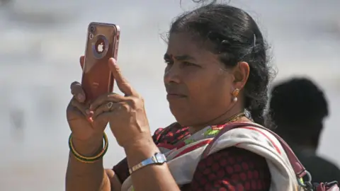 Getty Images A woman seen holding up a red smartphone with the apple logo