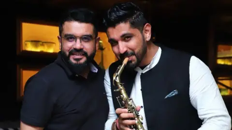 Saurabh Luthra/Instagram Saurabh Luthra (R), wearing a white shirt and holding the saxophone, stands with his brother Gaurav Luthra (L), who is wearing a black half sleeved shirt, for a picture. 