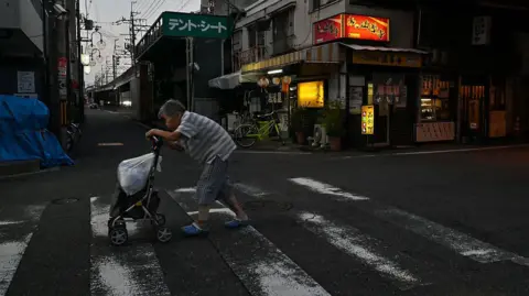 Getty Images An elderly woman crossing a dimly-lit street, pushing a stroller and a white plastic bag