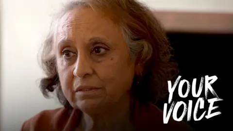 BBC Mina, a woman with grey, shoulder-length hair, pictured in a close-up portrait as she looks to the left of the camera. The BBC Your Voice branding is also on the image.