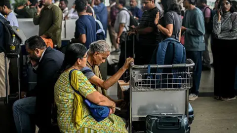 AFP via Getty Images Passengers wait near the IndiGo Airlines kiosk at the Chennai International Airport in Chennai on December 5, 2025. Chaos gripped Indian airports on December 4 after the country's biggest airline IndiGo cancelled over 1,200 flights, stranding thousands of passengers