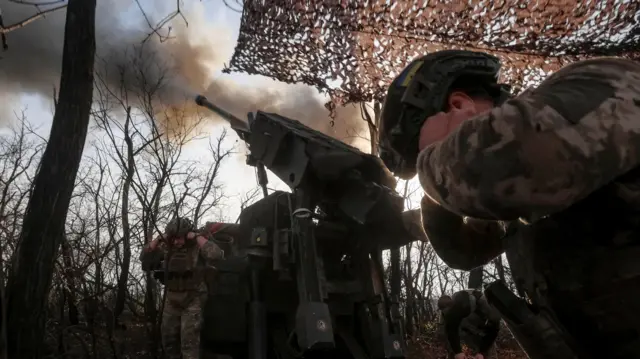 Two soldiers put their fingers in their ears as they fire a howitzer near Pokrovsk