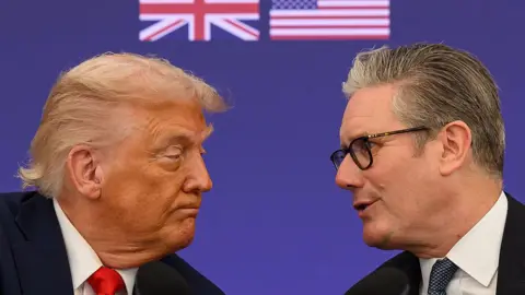Getty Images Close up of Trump on left and Starmer on right. They are facing each other. The background is purple and there is a partial US flag and British flag printed onto the background
