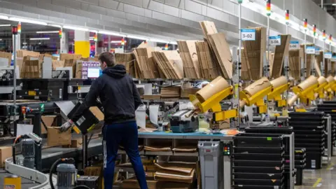 Getty Images A worker at a warehouse packages items as they pass him on a conveyor belt.