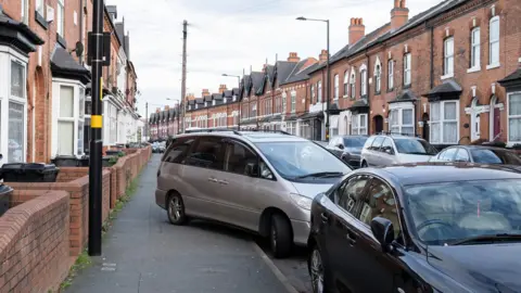 Getty Images A residential street in Birmingham showing a silver car partially parked on the pavement 