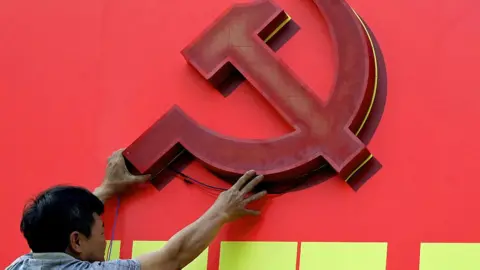 Getty Images A person reaches up to mount a large cutout of the hammer-and-sickle logo onto a red billboard