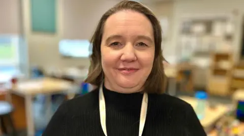 Martin Giles/BBC Steph Smith looking into camera in a classroom. She has shoulder-length brown hair and is wearing a black jumper with a white lanyard.
