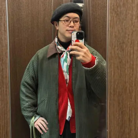Instagram/@detailance A man in a black beret and colourful scarf taking a photo in the mirror with his iPhone